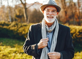 Older man in scarf and hat smiling outside