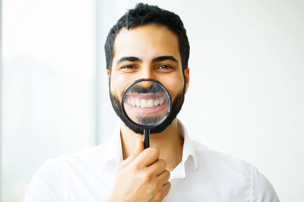man holding magnifying glass to smile after getting dental bonding in Pittsburgh