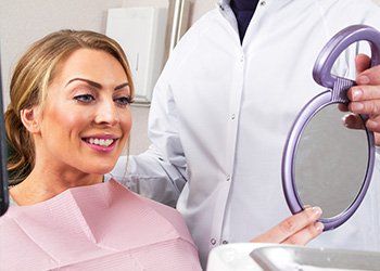 Woman looking at smile in mirror in dental chair