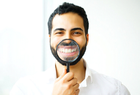 man in white shirt holding magnifying glass to his smile 
