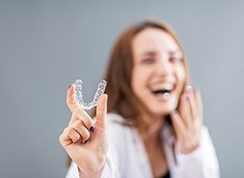 Woman laughing in background holding clear aligner to foreground