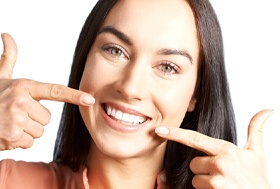 Woman pointing to her smile after full mouth reconstruction.