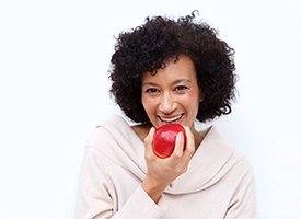 Woman with dental implants in Pittsburgh holding an apple