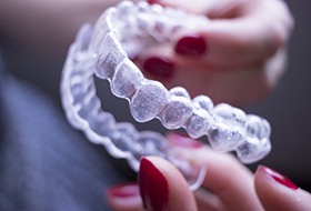 Fingers with red nail polish holding Invisalign trays