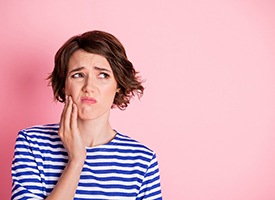 Woman in striped shirt touching jaw in pain with pink background