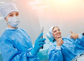 Dentist holding up extracted tooth with patient giving thumbs up in the background