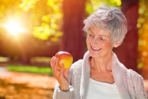 Woman with dentures in Pittsburg holding an apple and smiling 