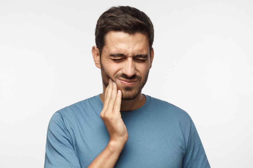 person experiencing tooth pain holding their cheek