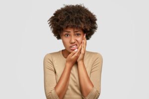 Woman in brown shirt holding her hands to her jaw in pain